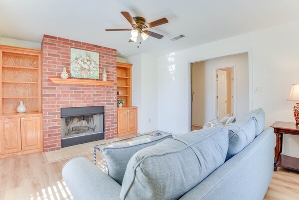 A living room with a brick fireplace, wooden shelves, a ceiling fan, and a light-colored sofa. - Relax Fireside! Poolside Oasis 3 Mi to Dtwn Sanger (Sanger)