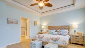 Een slaapkamer met een groot bed, twee nachtkastjes, een plafondventilator en een deur naar een andere kamer.