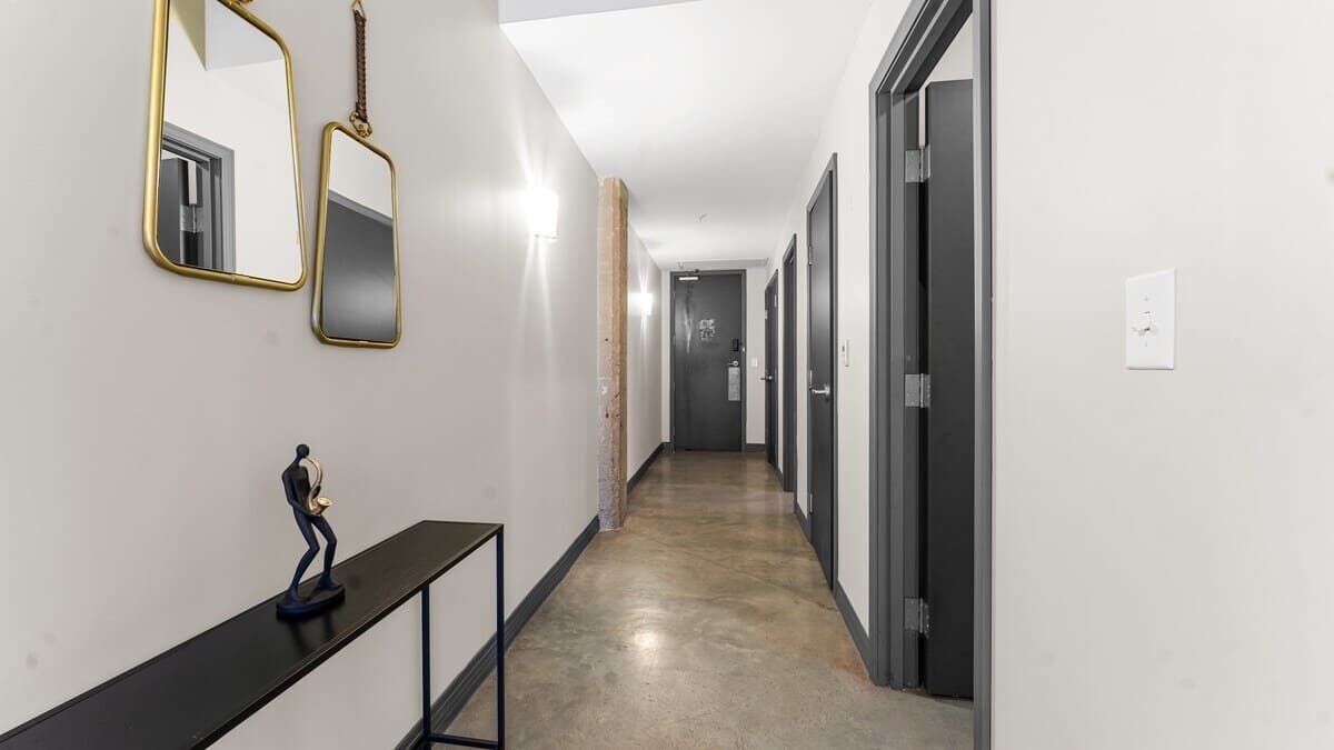 A hallway with a black console table, two wall-mounted mirrors, and a statue.