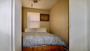 Quarto com cama, ventilador de teto, janela com persianas e quadro na parede.