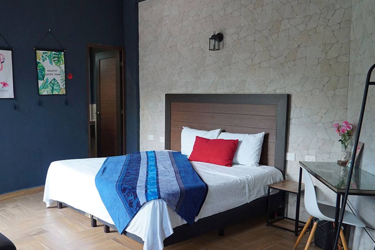 A bedroom with a bed, a nightstand, a chair, a table, and a door.
