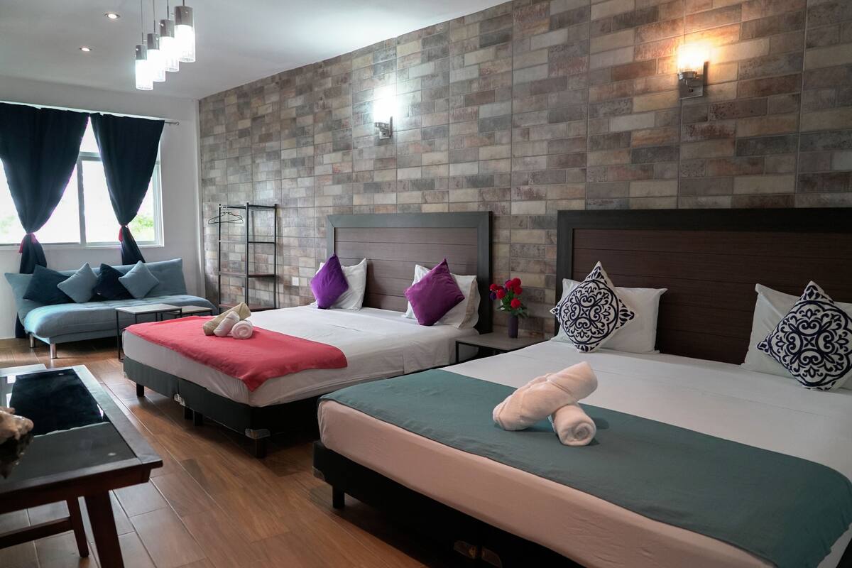 A hotel room with two beds, a sofa, a table, and a window with curtains.