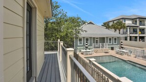A pool area with a wooden deck, a lounge with outdoor seating, and a building with a grey roof.