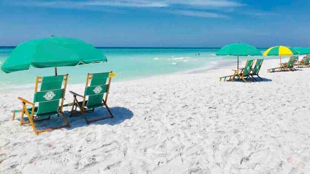 A beach with white sand and turquoise water. There are green and yellow beach chairs and umbrellas.