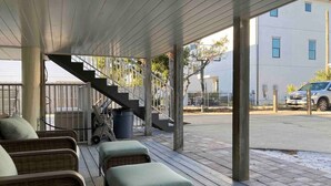 A covered outdoor seating area with wicker furniture and a staircase leading to an upper level.