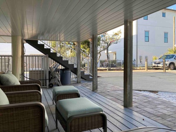 A covered outdoor seating area with wicker furniture and a staircase leading to an upper level.