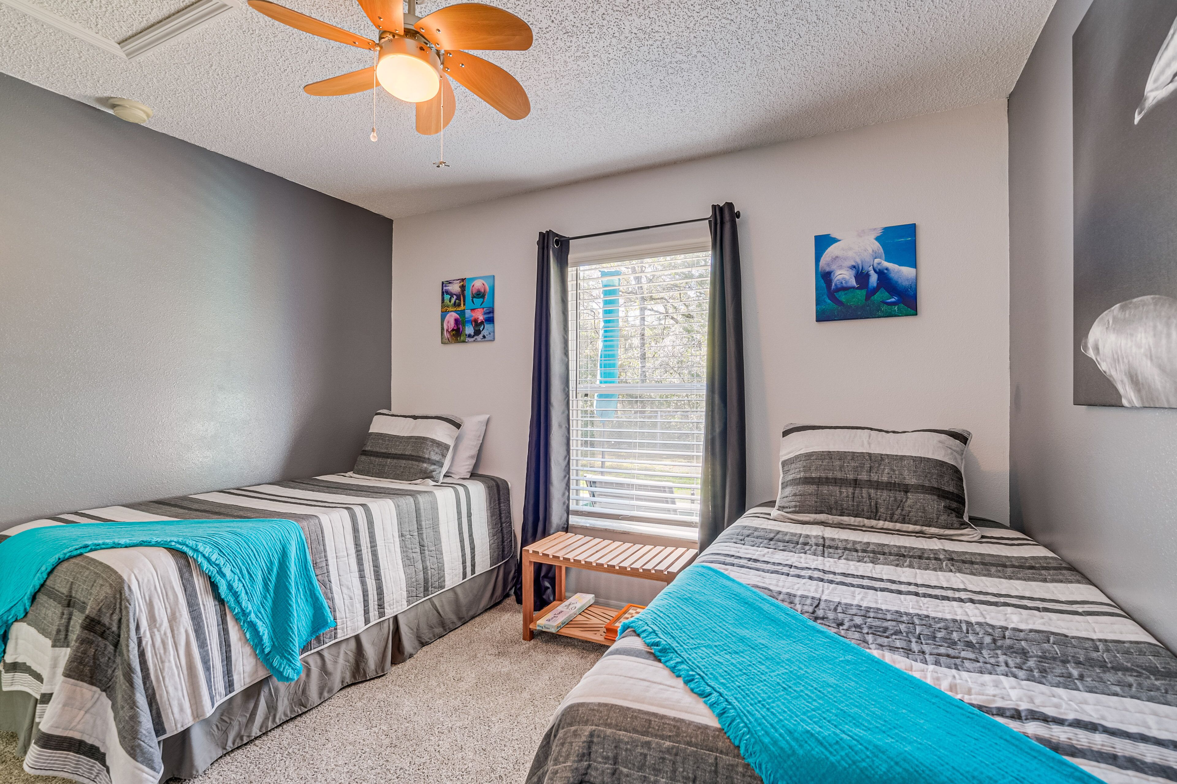 A bedroom with two single beds, a ceiling fan, a window with curtains, and wall art.