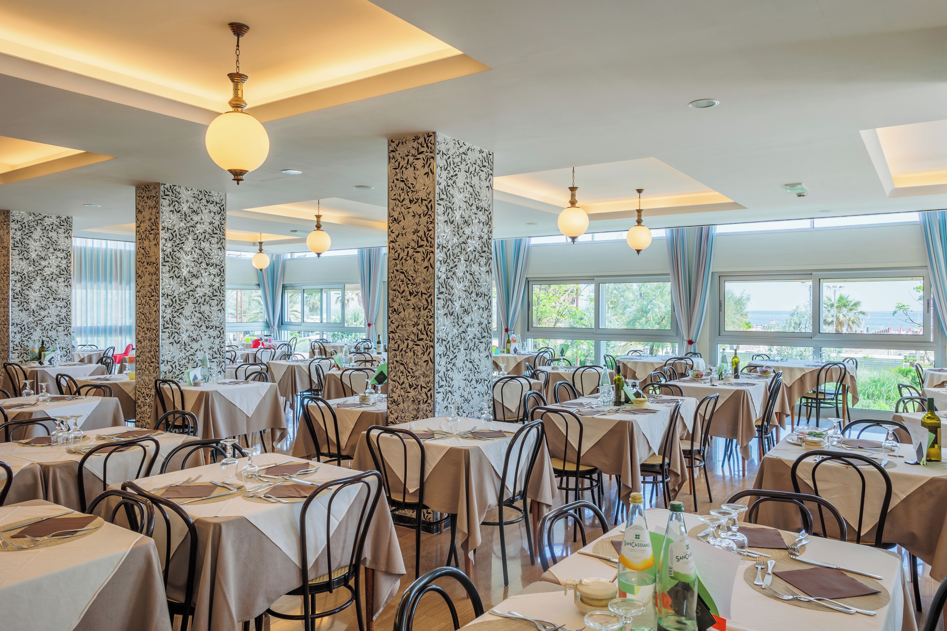 A restaurant with multiple tables, chairs, and hanging light fixtures.