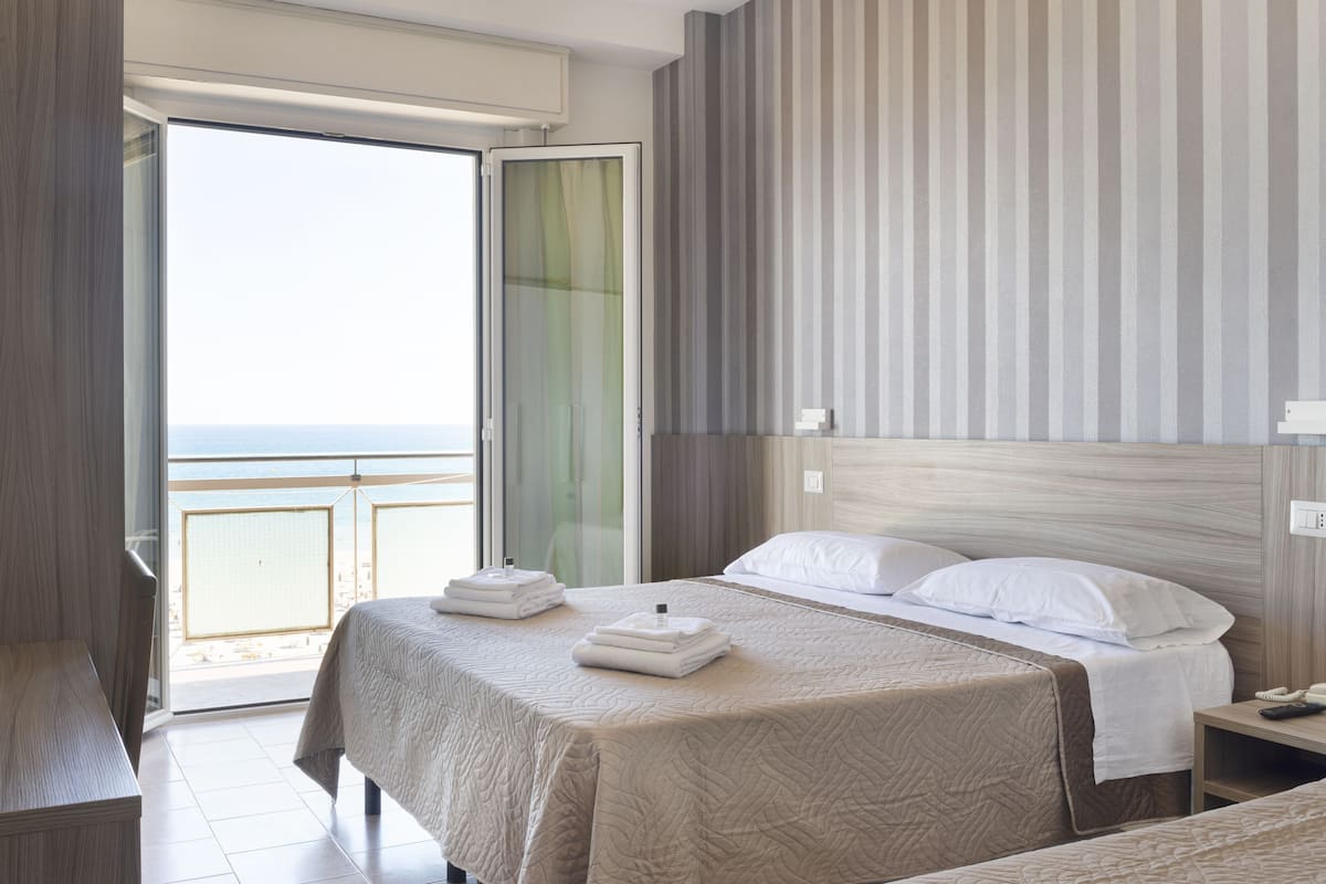 Habitación de hotel con dos camas, un balcón y vistas al mar.