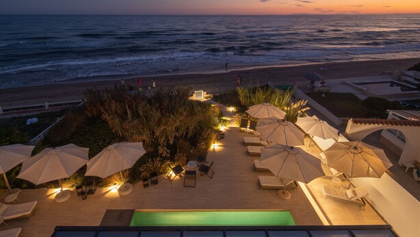 A poolside area with lounge chairs and umbrellas, overlooking a beach and ocean at sunset. - Villa Dune Costabella (Marbella)