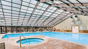 Une piscine intérieure dotée d’un toit en verre, d’un jacuzzi et d’un espace détente avec des chaises et des tables.