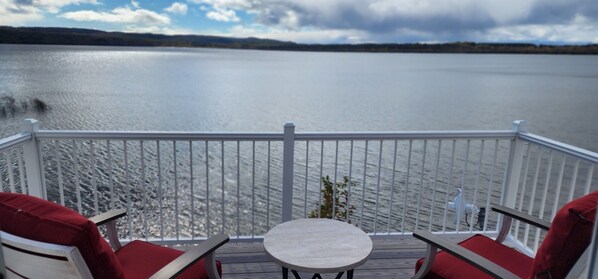 A balcony with a view of a calm lake, wooden deck, and red cushioned chairs. - Waterfront, AC, Newly Remodeled, Kayaks, 4 SUP, Rowboats (Frankfort)