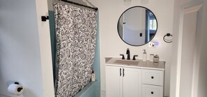 A bathroom with a patterned shower curtain, a round mirror, a sink with a soap dispenser, and cabinets. - Waterfront, AC, Newly Remodeled, Kayaks, 4 SUP, Rowboats (Frankfort)
