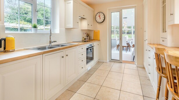 A modern kitchen with white cabinetry, a yellow kettle, and a dining area with a table and chairs. - The perfect larger family sized home with vast, lush, enclosed garden. (Trunch)