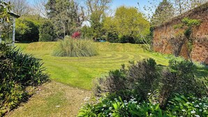 A well-maintained garden with a grassy lawn, various shrubs, and a brick wall. - The perfect larger family sized home with vast, lush, enclosed garden. (Trunch)