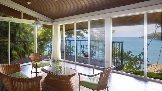 A sunlit room with wicker furniture, large windows, and a view of the sea. - One Bedroom Sea View Villa, Frenchman's Cove Resort (Drapers)