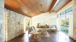 A spacious living area with a stone wall, wooden ceiling, and large windows. - One Bedroom Sea View Villa, Frenchman's Cove Resort (Drapers)