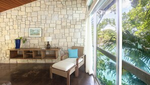 A room with a stone wall, a wooden ceiling, a bench, a chair, a table, and a view of greenery outside. - One Bedroom Sea View Villa, Frenchman's Cove Resort (Drapers)