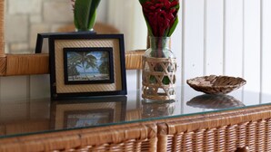 A wicker dresser with a mirror, a framed picture, and a vase with red flowers.