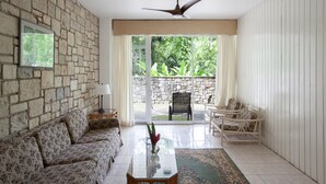 A living room with a stone wall, a ceiling fan, a sofa, a coffee table, and a view of greenery outside.