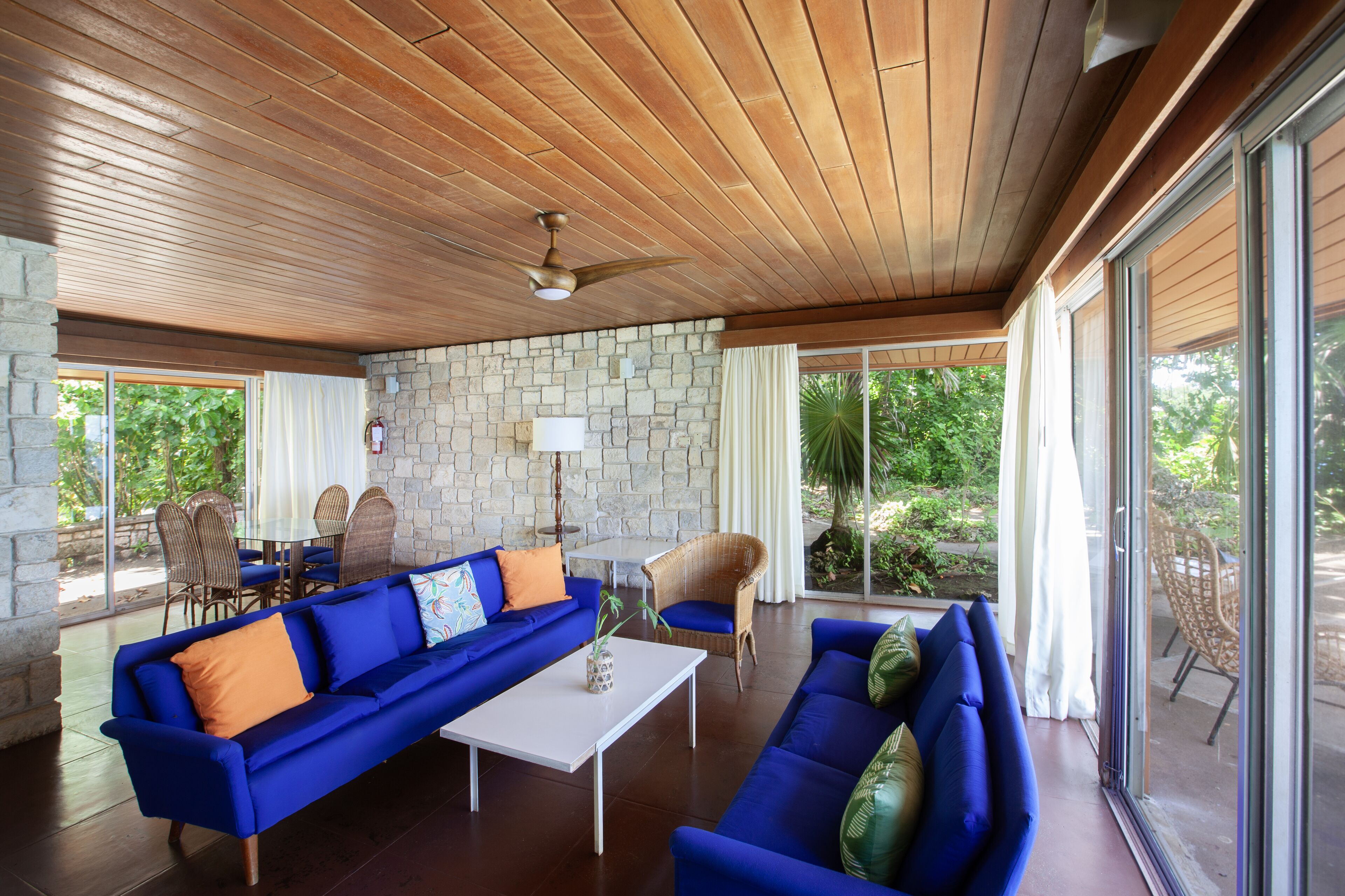 A spacious living area with a wooden ceiling, stone walls, and large windows offering a view of greenery.