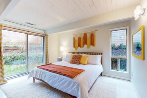 A bedroom with a large bed, a sliding glass door, and a view of the outdoors.