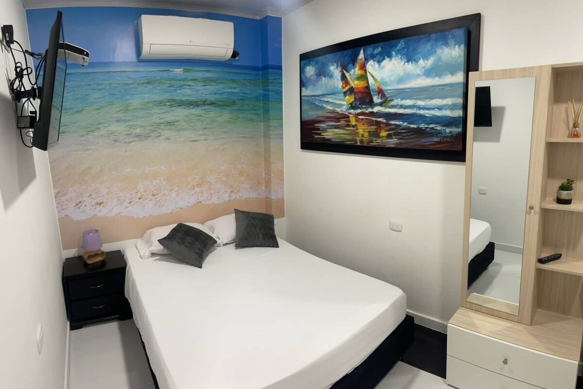 A bedroom with a bed, a nightstand, a dresser, a painting of a sailboat, and an air conditioning unit.