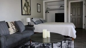 A modern bedroom with a grey sofa, a round coffee table with candles, a bed with a white duvet, and a painting on the wall. - Cincinnati Themed, Historic Big Sky Apartments! (Cincinnati)