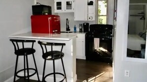A compact kitchen with white cabinets, a red microwave, and two black bar stools. - Cincinnati Themed, Historic Big Sky Apartments! (Cincinnati)