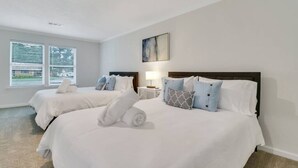 A hotel room with two beds, white bedding, a headboard, a bedside table with a lamp, and a window with blinds. - Hidden Gem in Pooler (Pooler)