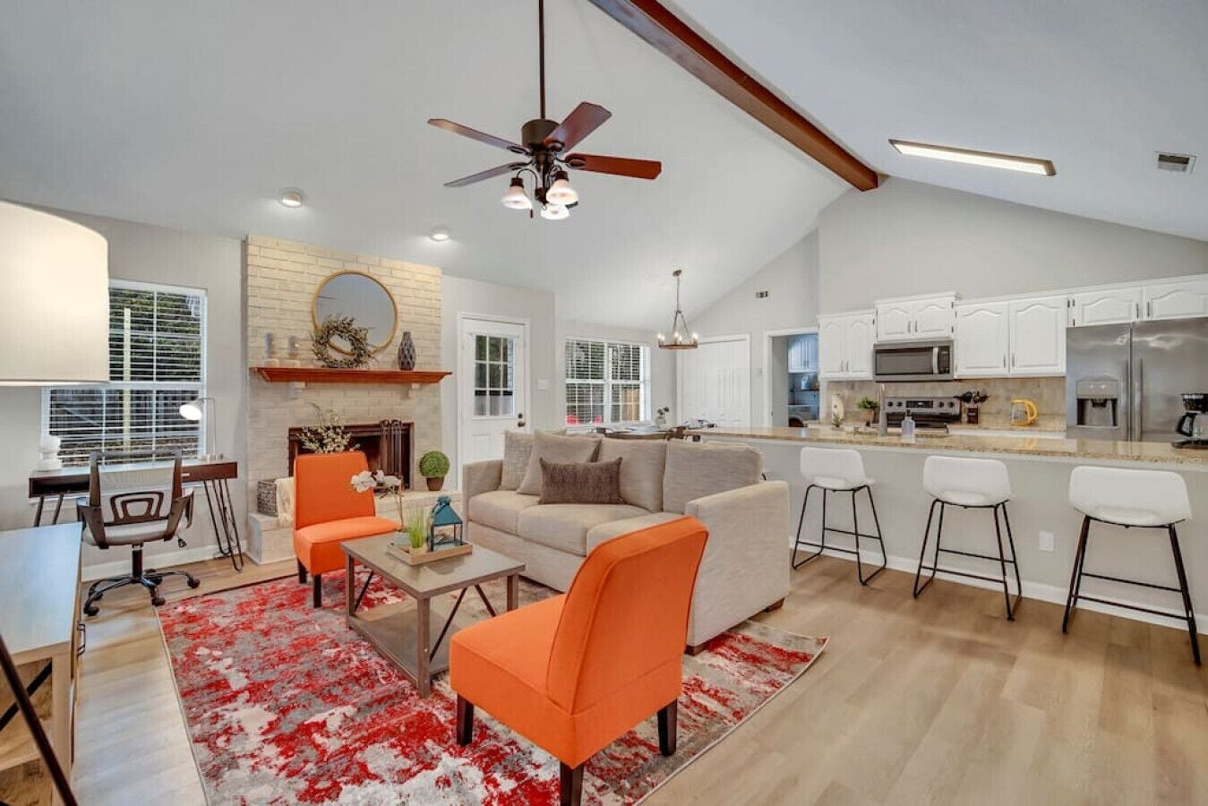 A spacious living room with a fireplace, a dining area, and a kitchen with white cabinets and a bar area.
