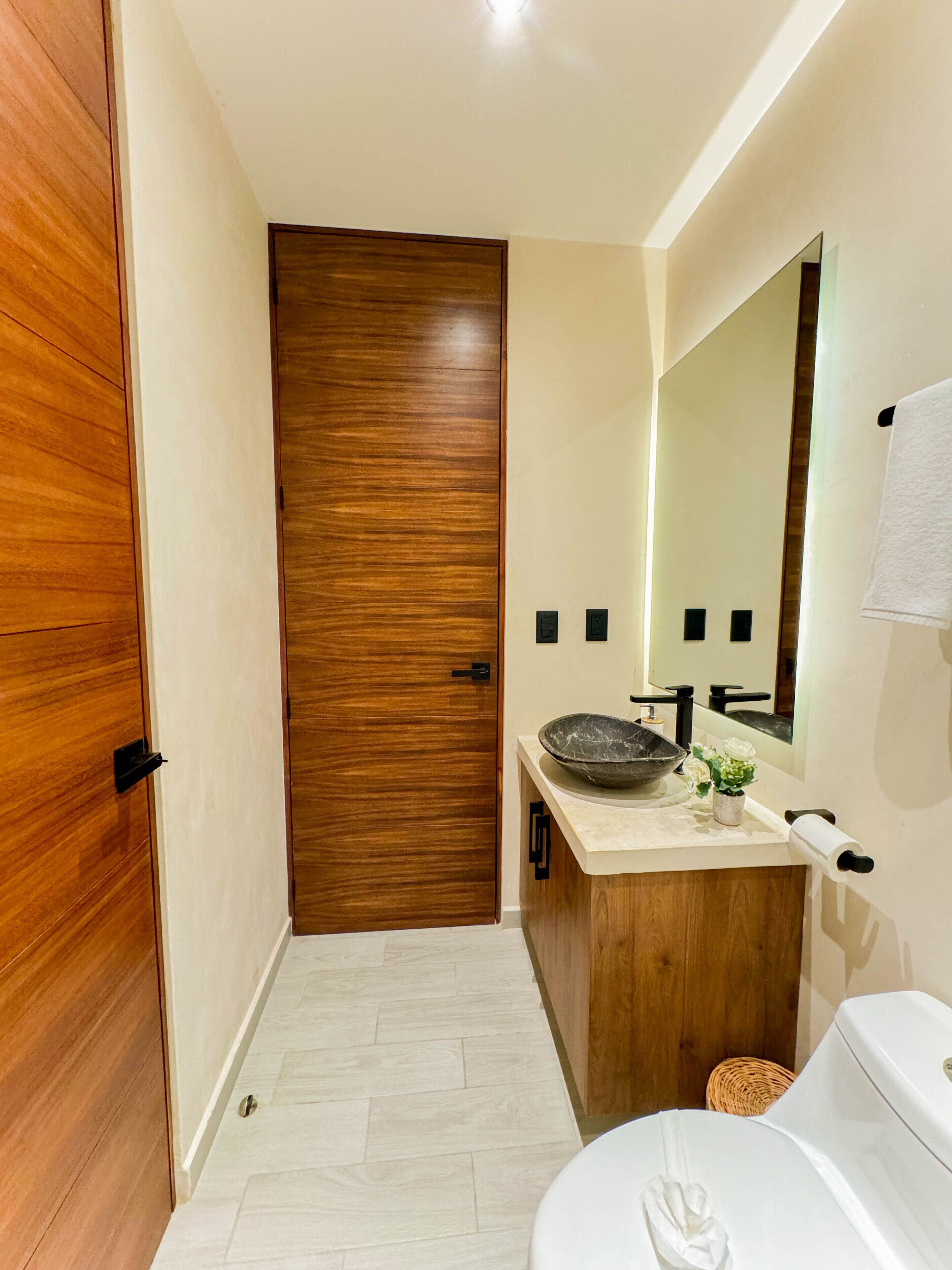 A bathroom with a wooden door, a sink with a large bowl, a mirror, and a toilet.