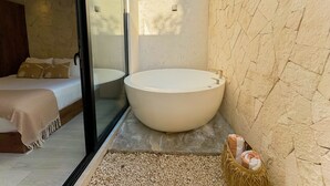 A modern bathroom with a large freestanding bathtub, a glass shower enclosure, and a bed with a beige blanket. - Tú Refugio Exclusivo en Tulum Dk Jade 3 (Tulum)