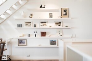 A room with white walls and a staircase. There are several shelves with framed pictures and decorative items.