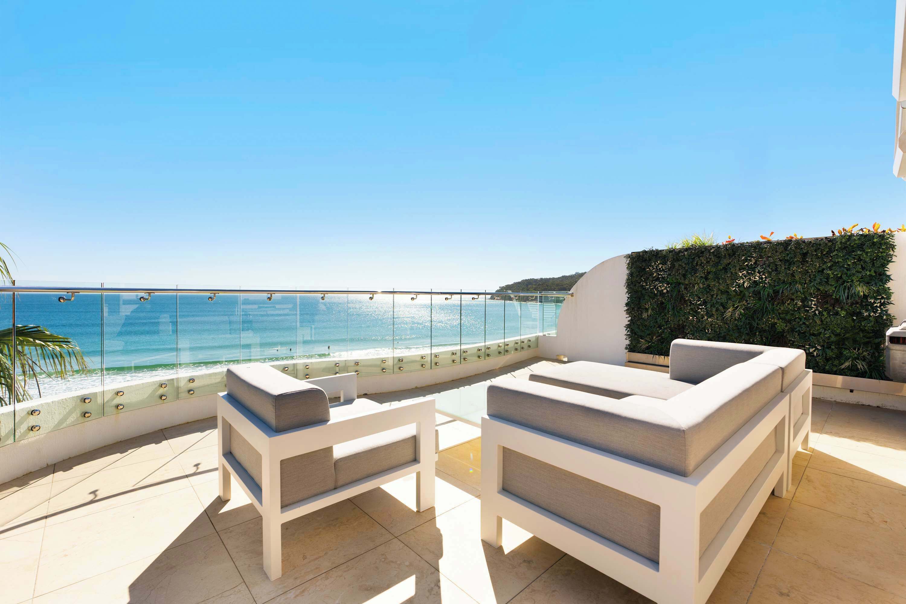 A terrace with white furniture, a glass balustrade, and a view of the sea.