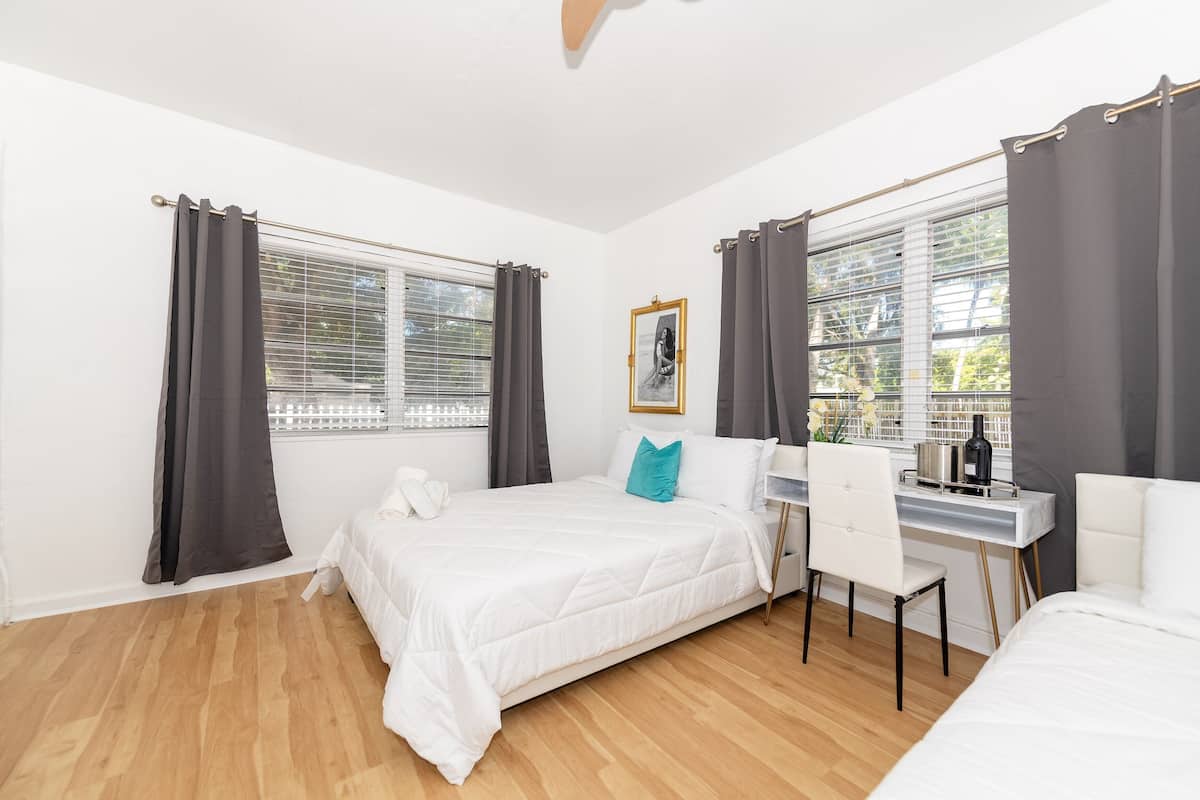 Une chambre moderne comprenant un lit, un bureau et une chaise, avec une grande fenêtre agrémentée de rideaux et un tableau encadré accroché au mur.