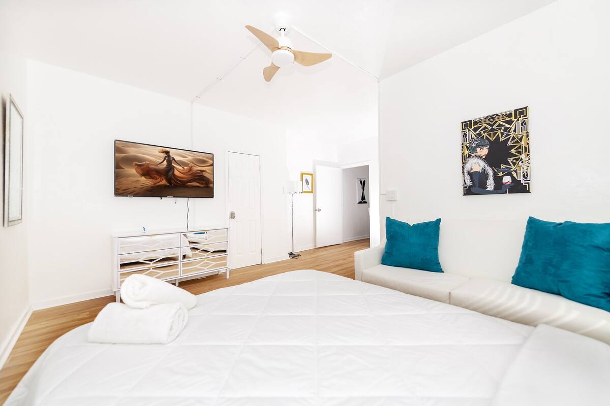 Une chambre d’hôtel moderne avec un grand lit, des murs blancs, un ventilateur de plafond, une télévision et des œuvres d’art.