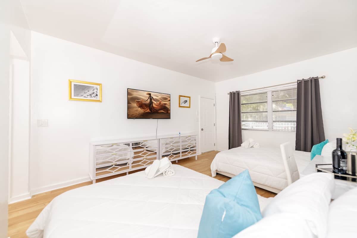 Une chambre d’hôtel avec deux lits, un ventilateur de plafond, une fenêtre avec des rideaux et des œuvres d’art accrochées aux murs.