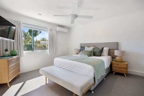 A bedroom with a bed, bedside tables, a bench, a ceiling fan, and a window with curtains.