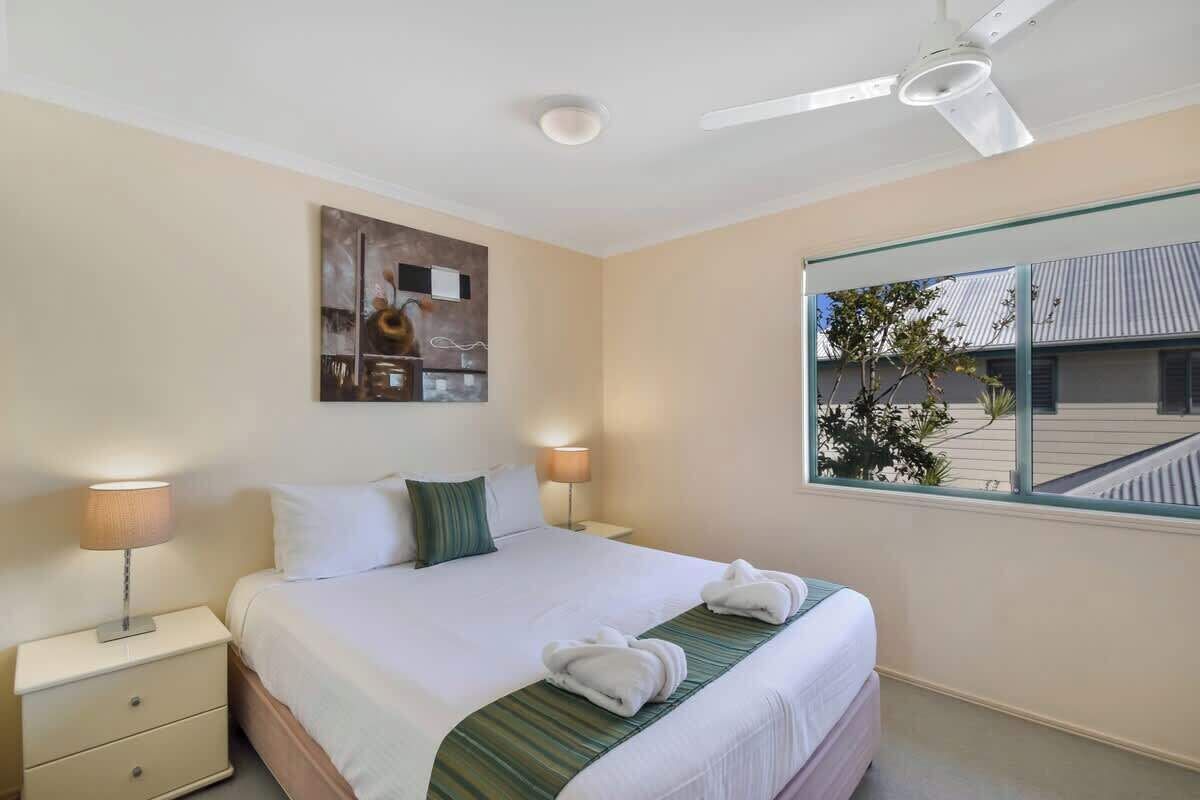 Camera d'albergo con un letto, due lampade da comodino, una ventola a soffitto, una finestra con vista sull'esterno e un'opera d'arte appesa al muro.