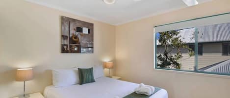 Camera d'albergo con un letto, due lampade da comodino, una ventola a soffitto, una finestra con vista sull'esterno e un'opera d'arte appesa al muro.