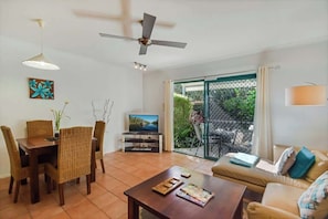 A living room with a TV, dining table, chairs, a sofa, and a ceiling fan.