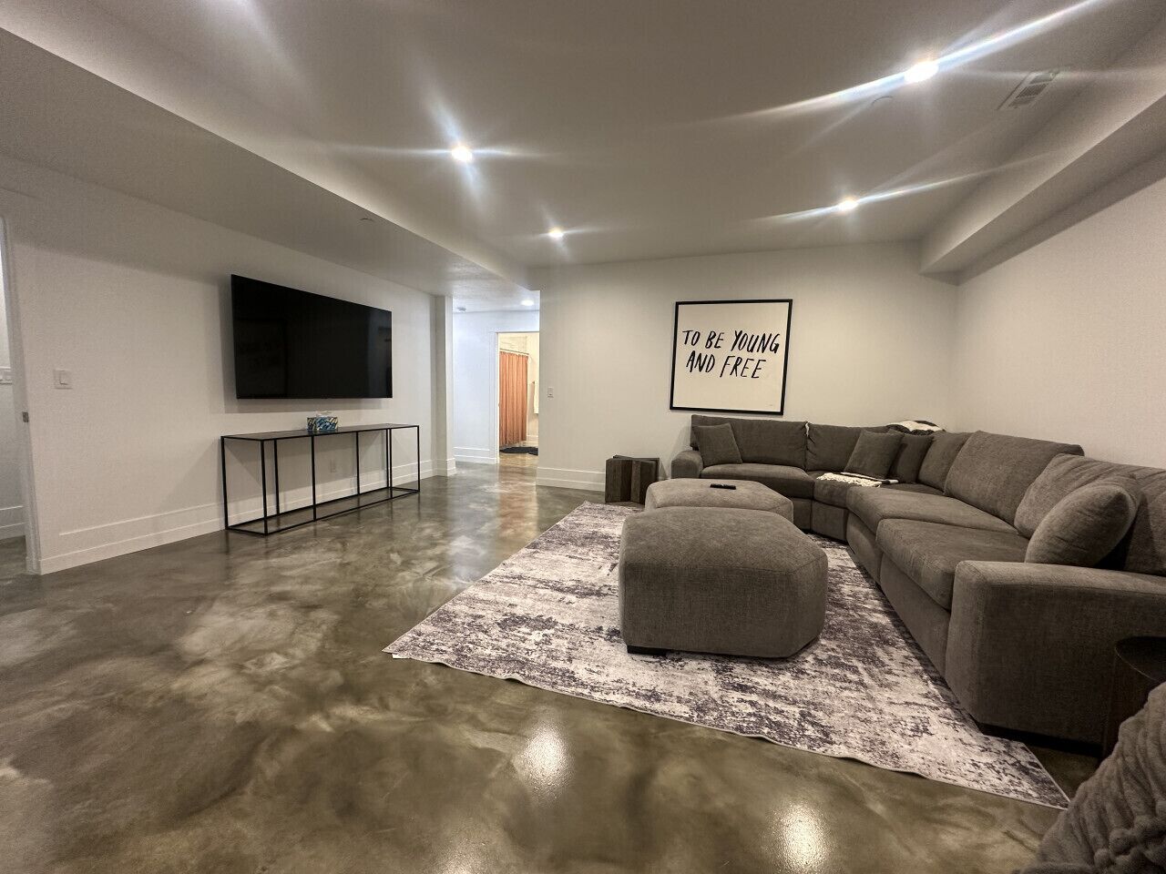 Ein geräumiges Wohnzimmer mit einer großen Eckcouch, einem flachbildfernseher an der Wand und einem minimalistischen Design.