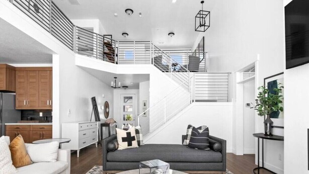 Ein großzügiger Wohnbereich mit grauem Sofa, einem weißen Coucheck und einem runden Couchtisch. Eine Treppe führt zu einer oberen Ebene.