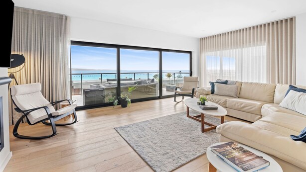 A modern living room with a large sliding glass door leading to a balcony with a view of the sea. - Oceania 8 (Lorne)