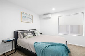 A bedroom with a bed, a bedside table, a wall-mounted air conditioner, a window, and a framed picture on the wall. - Oceania 8 (Lorne)
