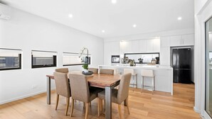 A modern kitchen with white cabinets, a black refrigerator, and a wooden dining table with chairs. - Oceania 8 (Lorne)