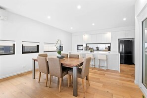 A modern kitchen with white cabinets, a black refrigerator, and a wooden dining table with chairs. - Oceania 8 (Lorne)