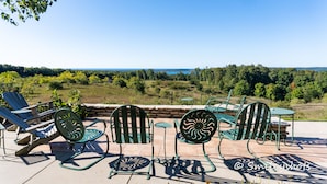 A patio with outdoor furniture, including chairs and a table, overlooking a scenic landscape with trees and a body of water. - Large Historic Home with views of Crystal Lake & Lake Michigan (Frankfort)