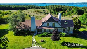 A two-story house with a stone foundation, a red roof, and a chimney. It is surrounded by a well-maintained lawn and a stone pathway leading to the entrance. - Large Historic Home with views of Crystal Lake & Lake Michigan (Frankfort)